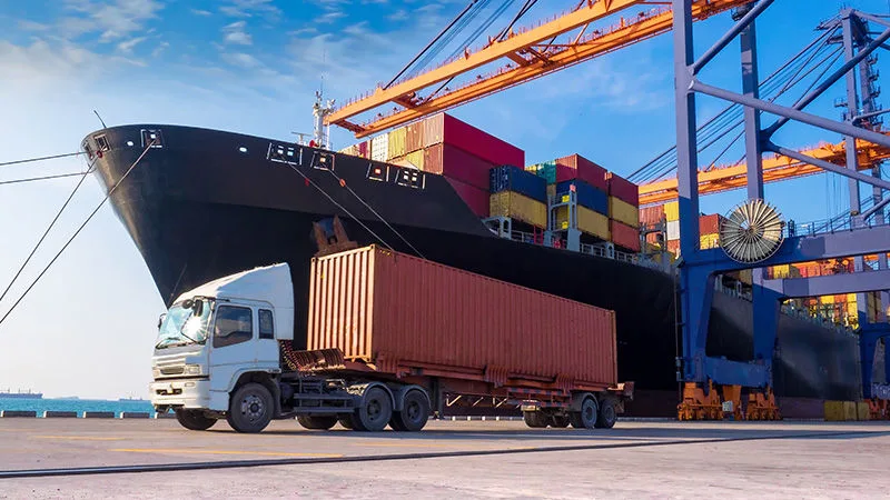 Cargo ship and container truck at port for international shipping by Quick Exim.